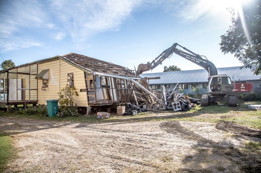 A House Is Being Demolished By A Large Excavator — Integrabuild in Bowen, QLD