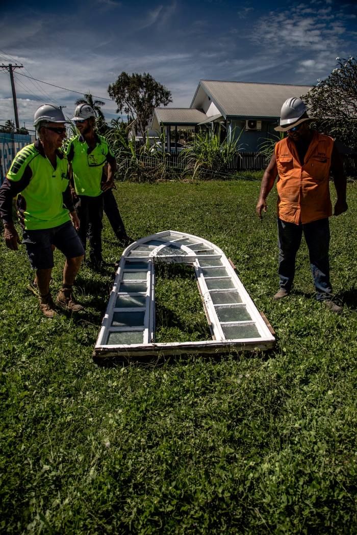 A Group Of Construction Workers Are Standing In A Grassy Field Looking At A Ladder — Integrabuild in Proserpine, QLD