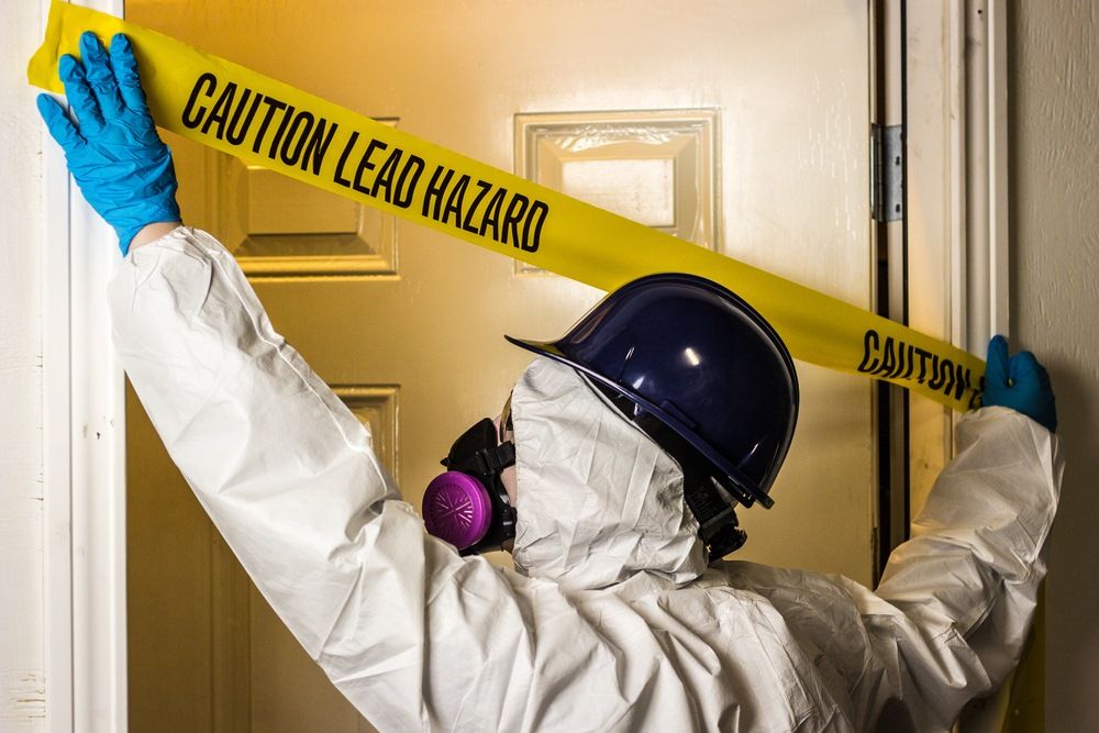 A Person In A Protective Suit Is Holding A Caution Lead Hazard Tape On A Door — Integrabuild in Proserpine, QLD