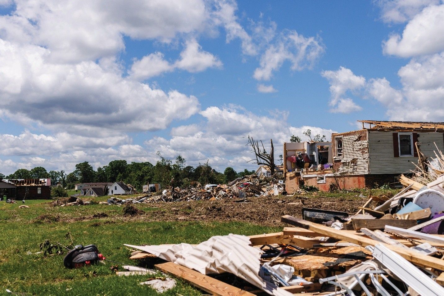 Tornado damage: debris-strewn field with damaged homes under a partly cloudy sky.