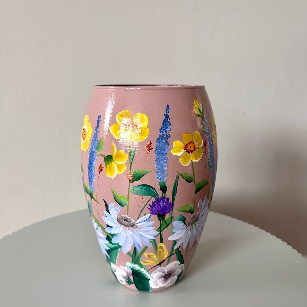 Een vaas met een mauve achtergrond, beschilderd met een levendig boeket gele, paarse en witte wilde bloemen.