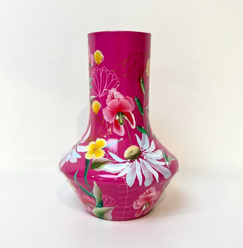 Een magentakleurige vaas met een brede voet en een smalle hals, versierd met geschilderde witte roze en gele bloemen.