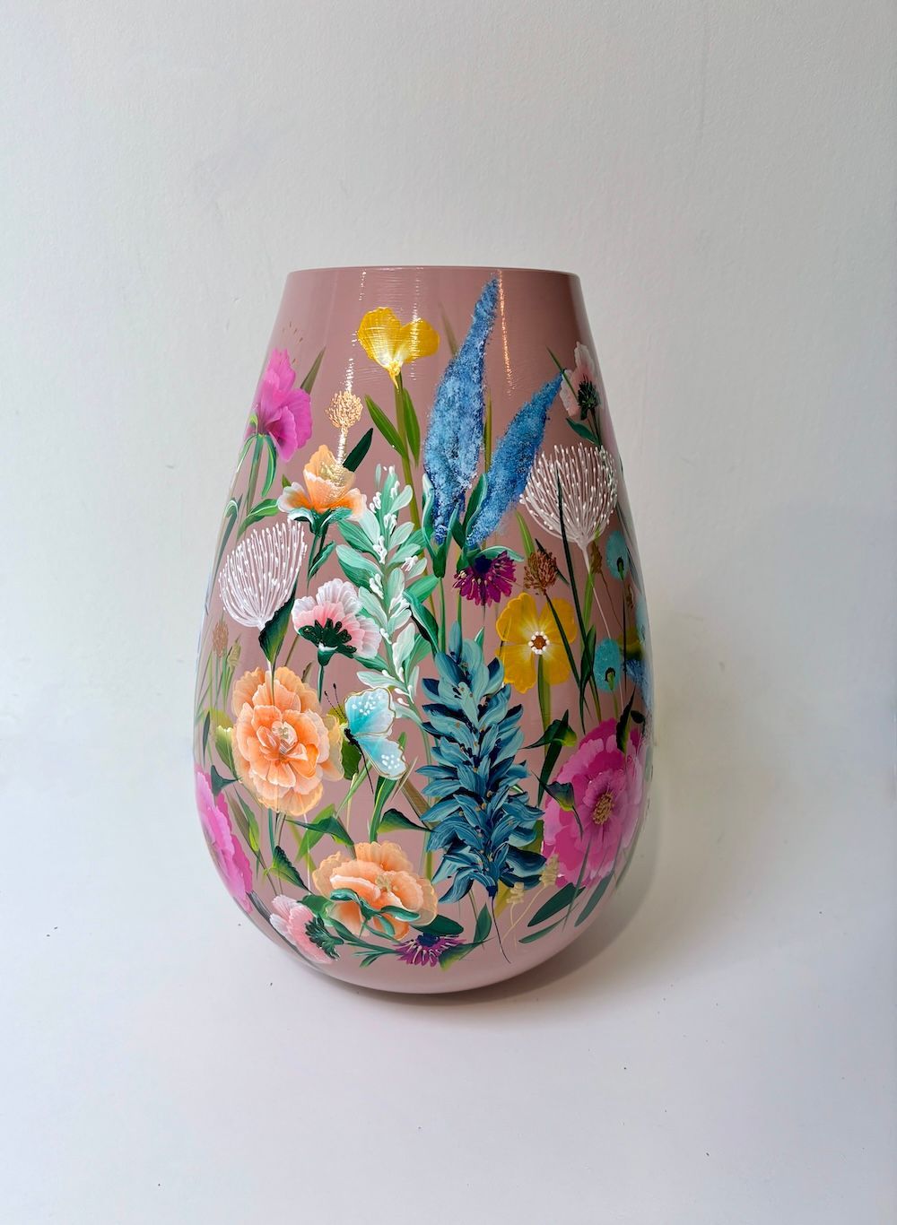 Roze vaas met kleurrijke bloemen- en vlinderschilding op een witte achtergrond.