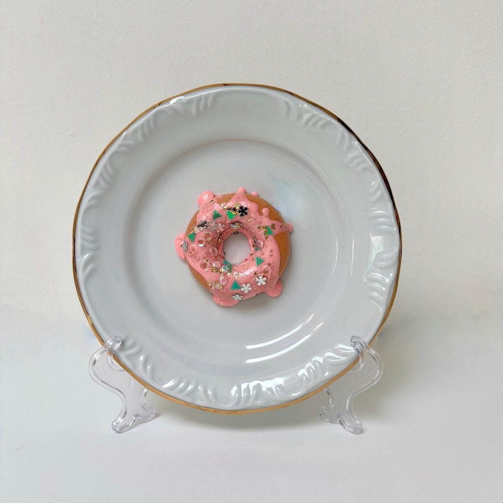 Een roze geglazuurde donut met kleurrijke spikkels ligt in het midden van een wit bord met een gouden rand