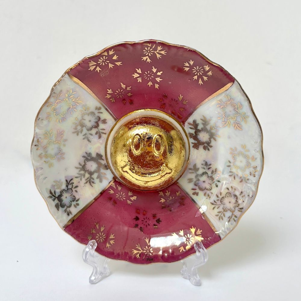 Een decoratief porseleinen schoteltje met afwisselend bordeauxrode en witte bloemmotieven en een verguld middenstuk.