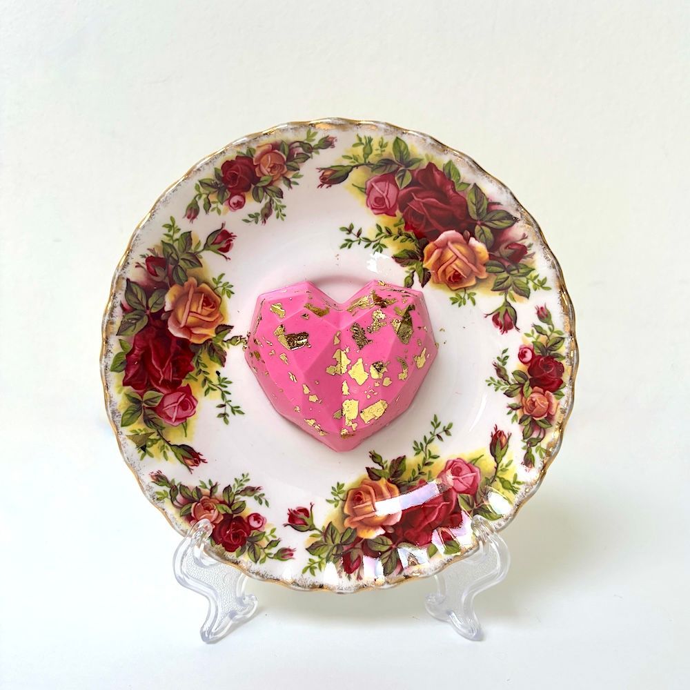 Een geometrisch, goudkleurig roze hart rust op een vintage-achtig bord met een geschulpte rand