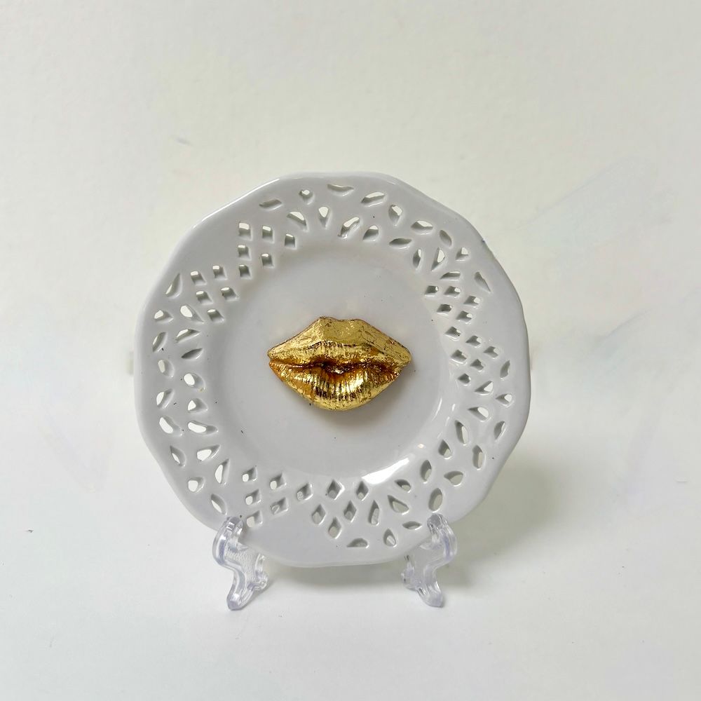 Een wit porseleinen decoratief bord met een rastervormige rand en een  gestructureerd goudkleurig lippen in het midden.