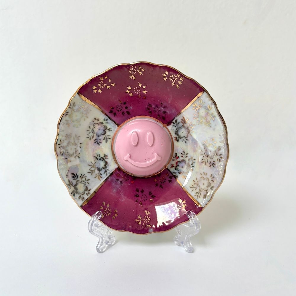 Een decoratief bord met afwisselende magenta en witte bloemmotieven, met in het midden een roze smiley.