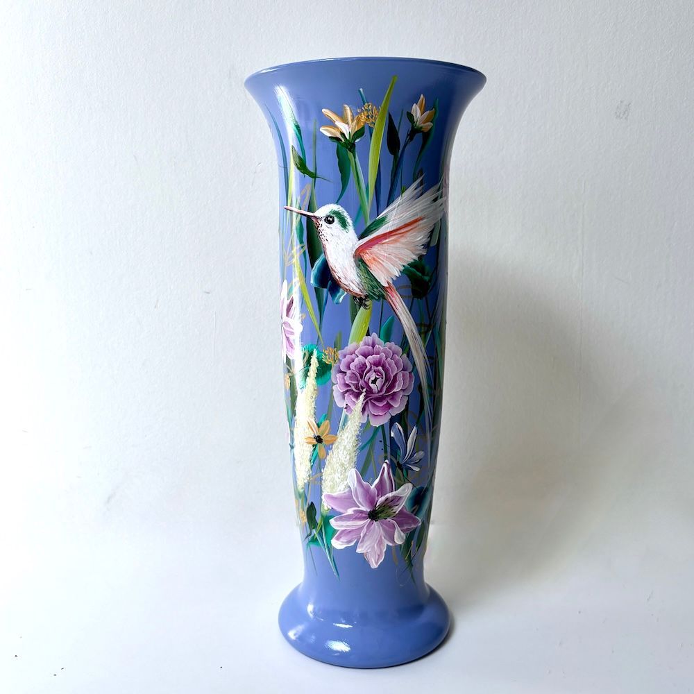 Blauwe keramische vaas met geschilderde kolibrie en roze bloemen.