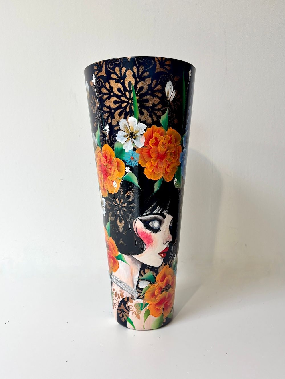 Een vaas versierd met een bloemenpatroon, gouden kantachtige accenten en een profielillustratie van een gestileerde figuur.