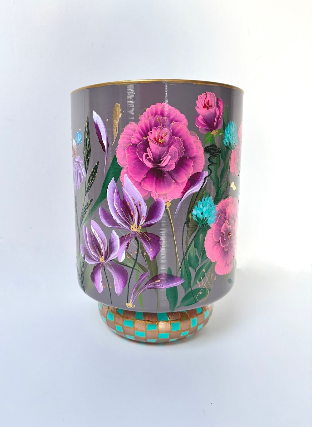 Een grijze vaas, beschilderd met  bloemen en groene bladeren, staat op een voetstuk met een patroon in turquoise en goud.