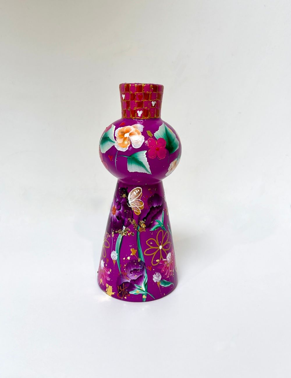 Een paarse, handbeschilderde kaarsenhouder met bloemmotieven en een rood-gouden geplaatst op een witte ondergrond.
