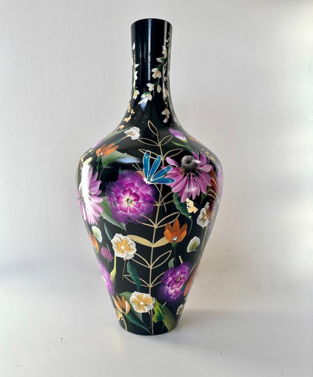 Een zwarte glazen vaas versierd met felpaarse bloemen, witte bloesems en een kleurrijke kolibrie.