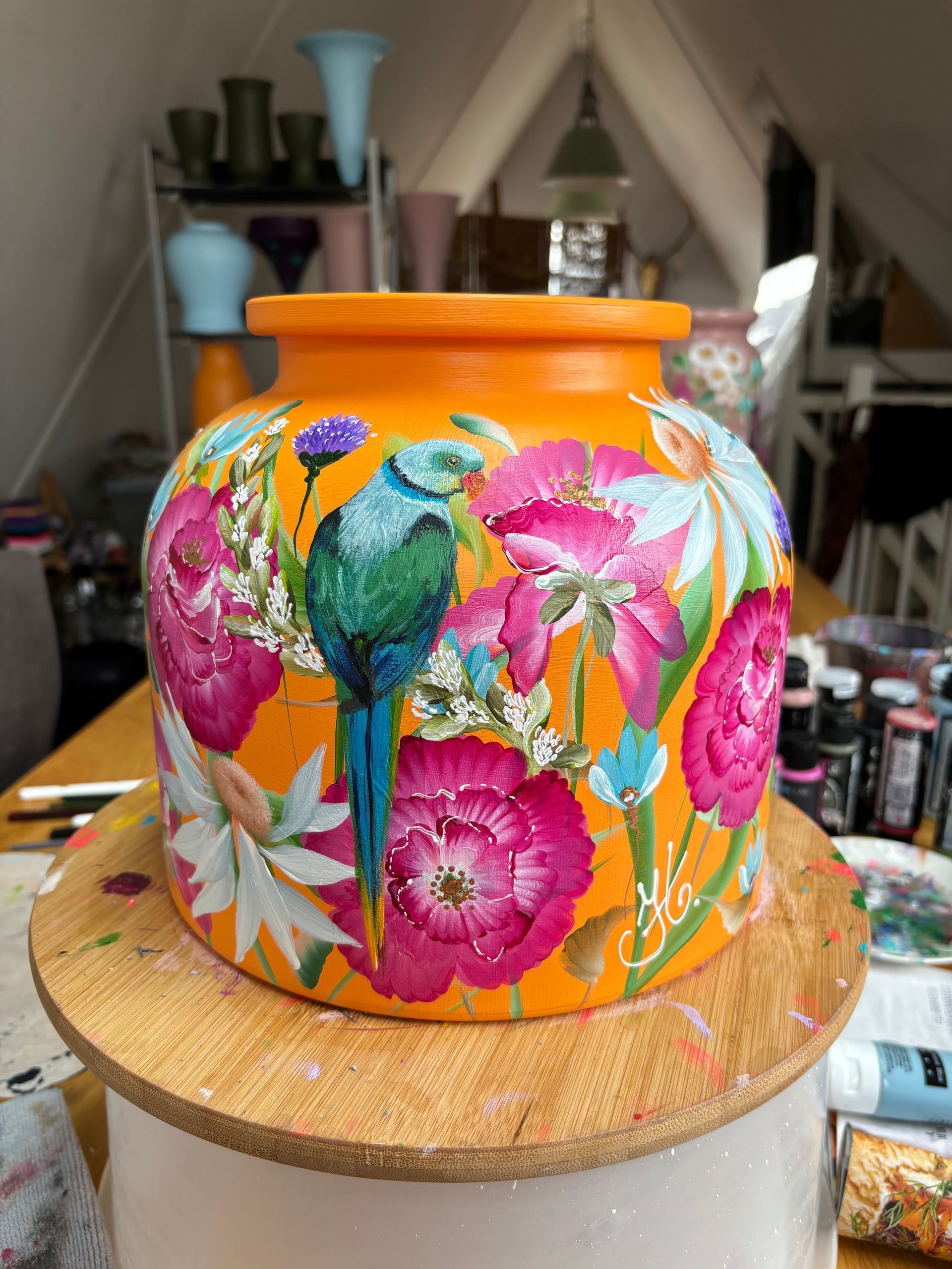 Een levendige oranje keramische pot, handbeschilderd met een turquoise tropische vogel met felroze bloemen en witte blaadjes.