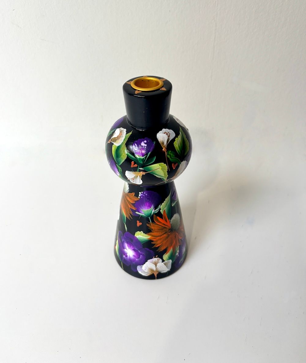 Een zwarte houten kandelaar, beschilderd met een levendig bloemenpatroon op een witte ondergrond.