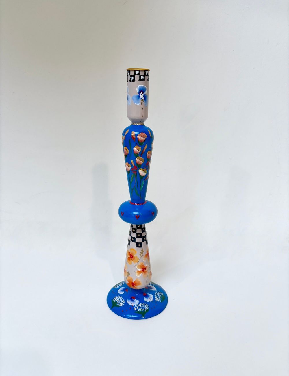 Een kleurrijke, gelaagde kandelaar met bloemenmotieven, ruitjesaccenten en een blauwe voet op een witte achtergrond.