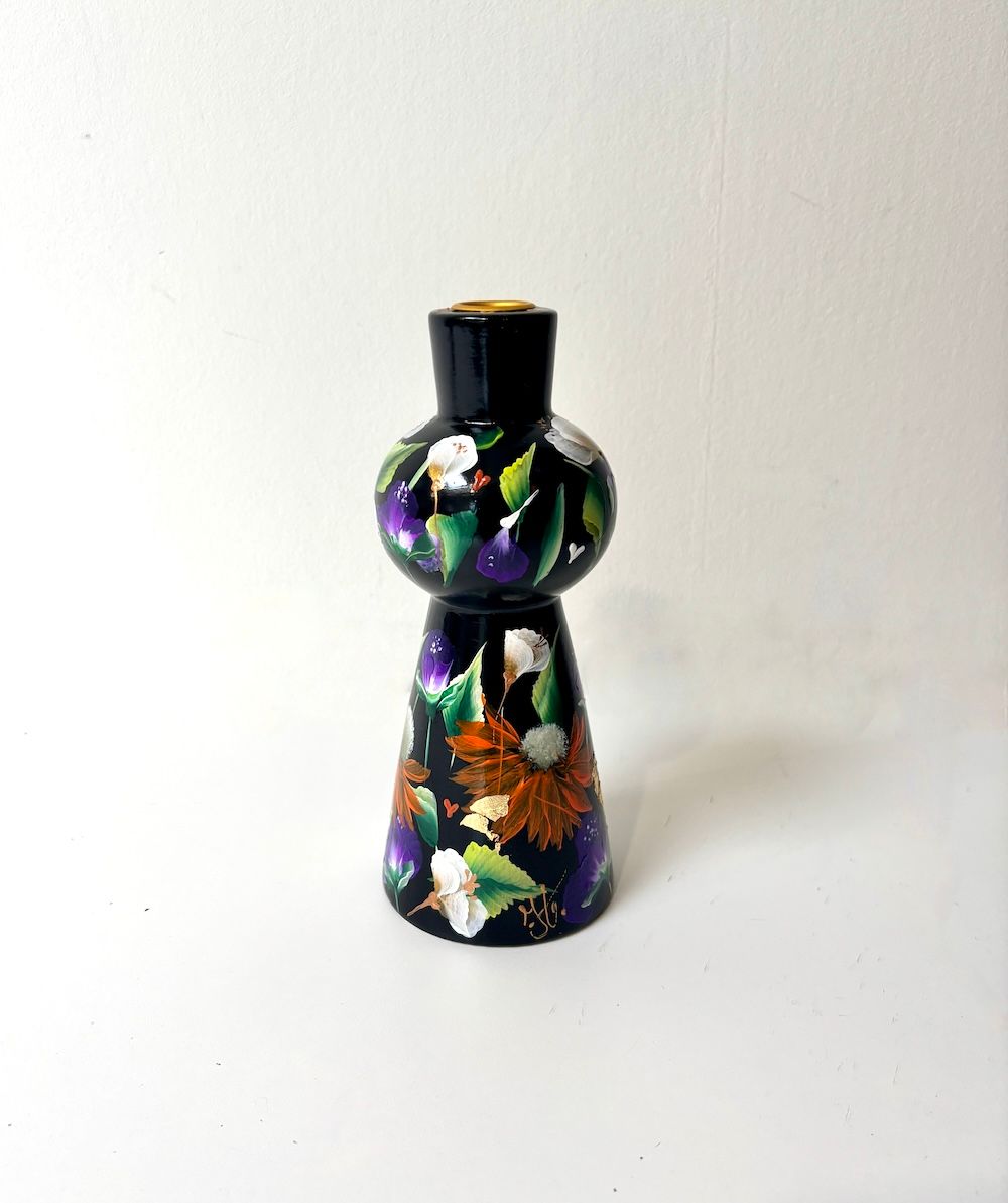 Een zwarte houten kandelaar, beschilderd met een levendig bloemenpatroon op een witte ondergrond.