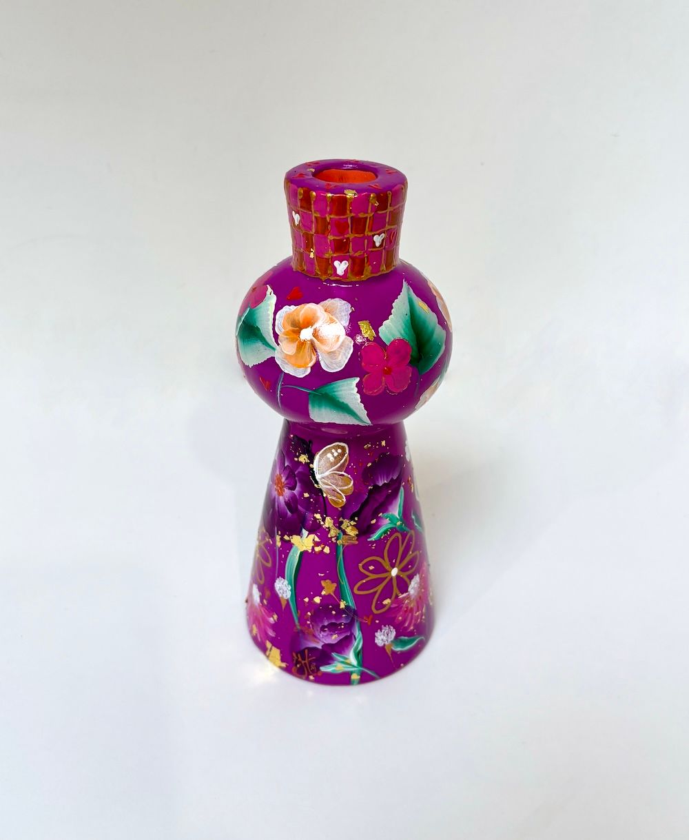 Een paarse, handbeschilderde kaarsenhouder met bloemmotieven en een rood-gouden geplaatst op een witte ondergrond.