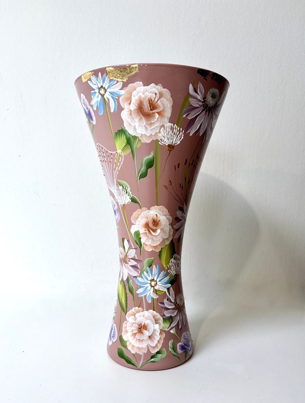 Een lichtbruine, zandlopervormige vaas, beschilderd met een kolibrie, diverse kleurrijke bloemen en accenten van bladgoud.