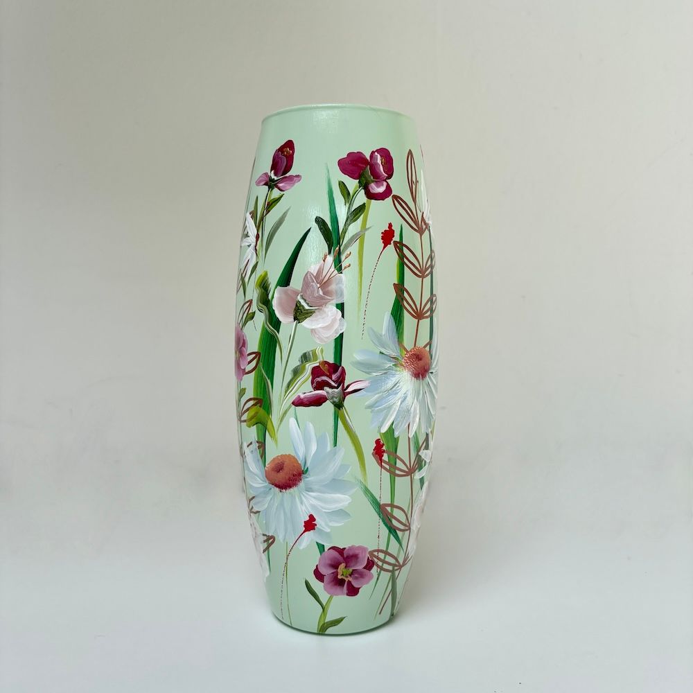Een lichtgroene cilindrische vaas, handbeschilderd met witte madeliefjes, paarse bloemen en delicate groene stengels.