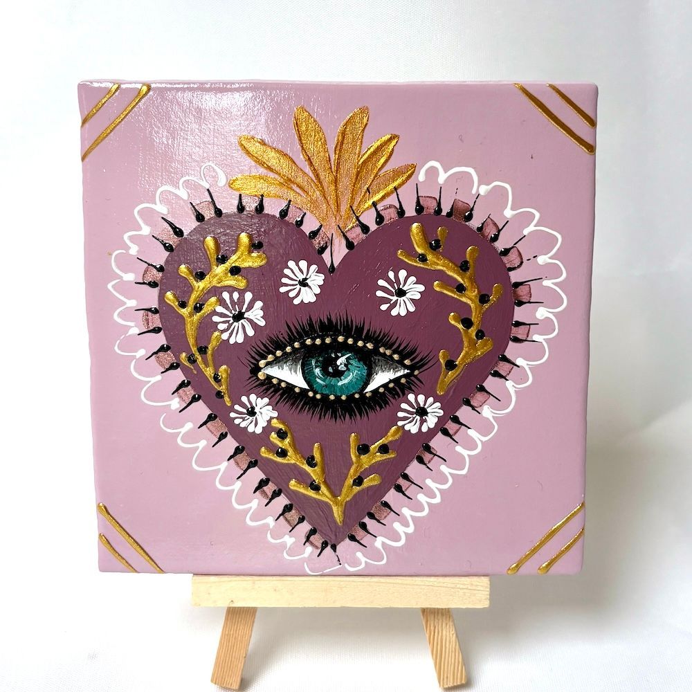 Roze canvas met een ontwerp van een hart en oog bezet met juwelen, op een kleine houten schildersezel.