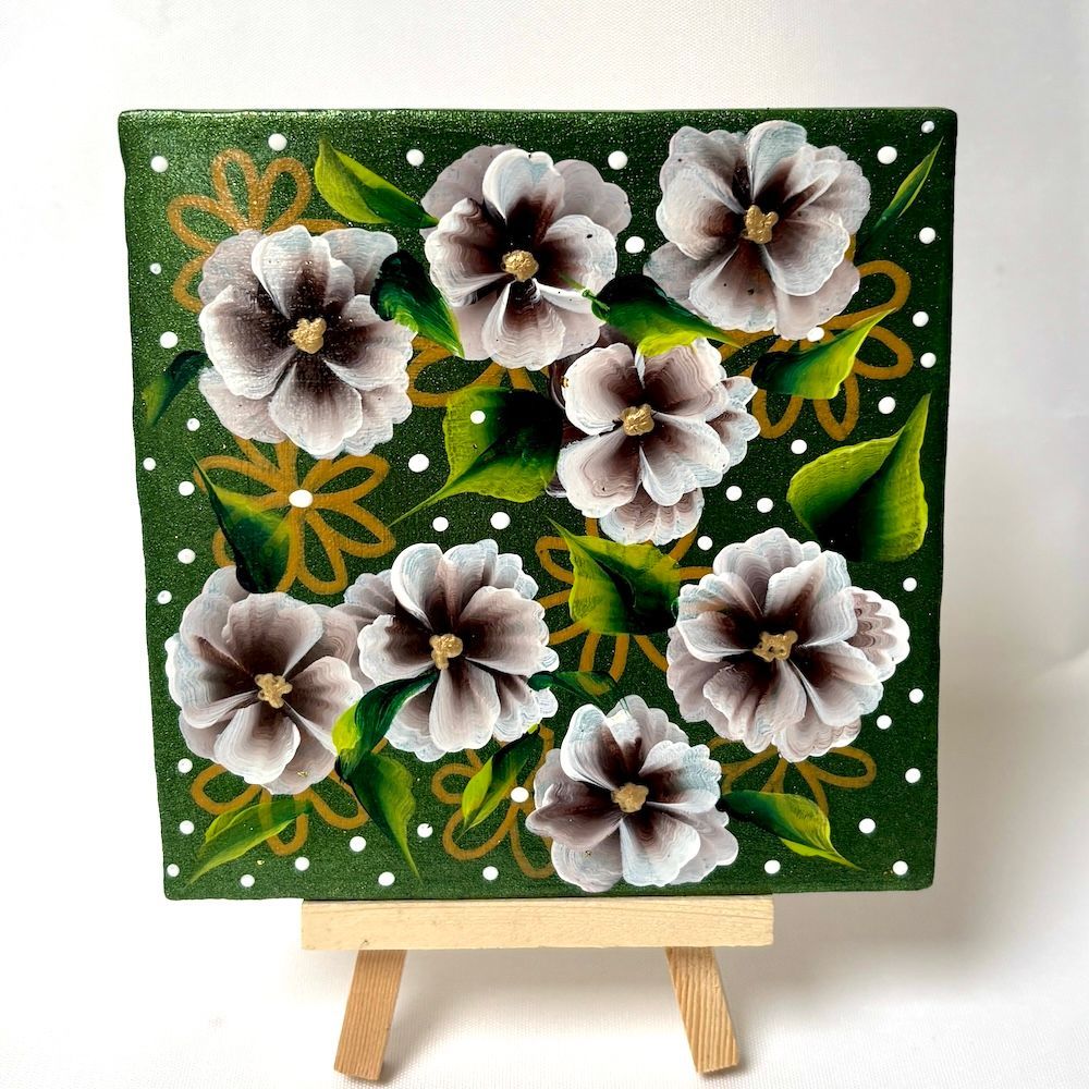 Een klein, vierkant tegeltje met witte bloemen met donkere centra op een glinsterende groene achtergrond,