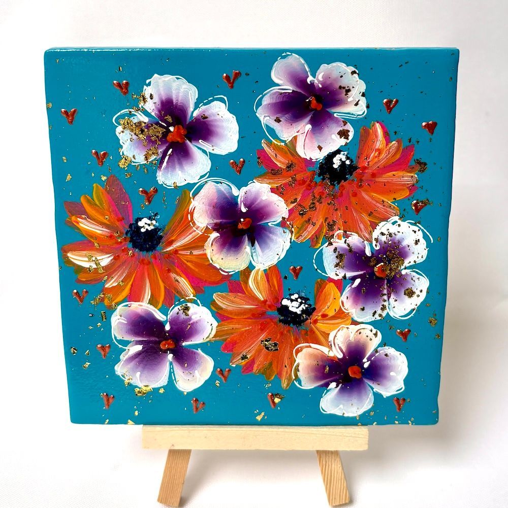 Kleurrijk bloemenschilderij op een blauw canvas, tentoongesteld op een kleine houten schildersezel.