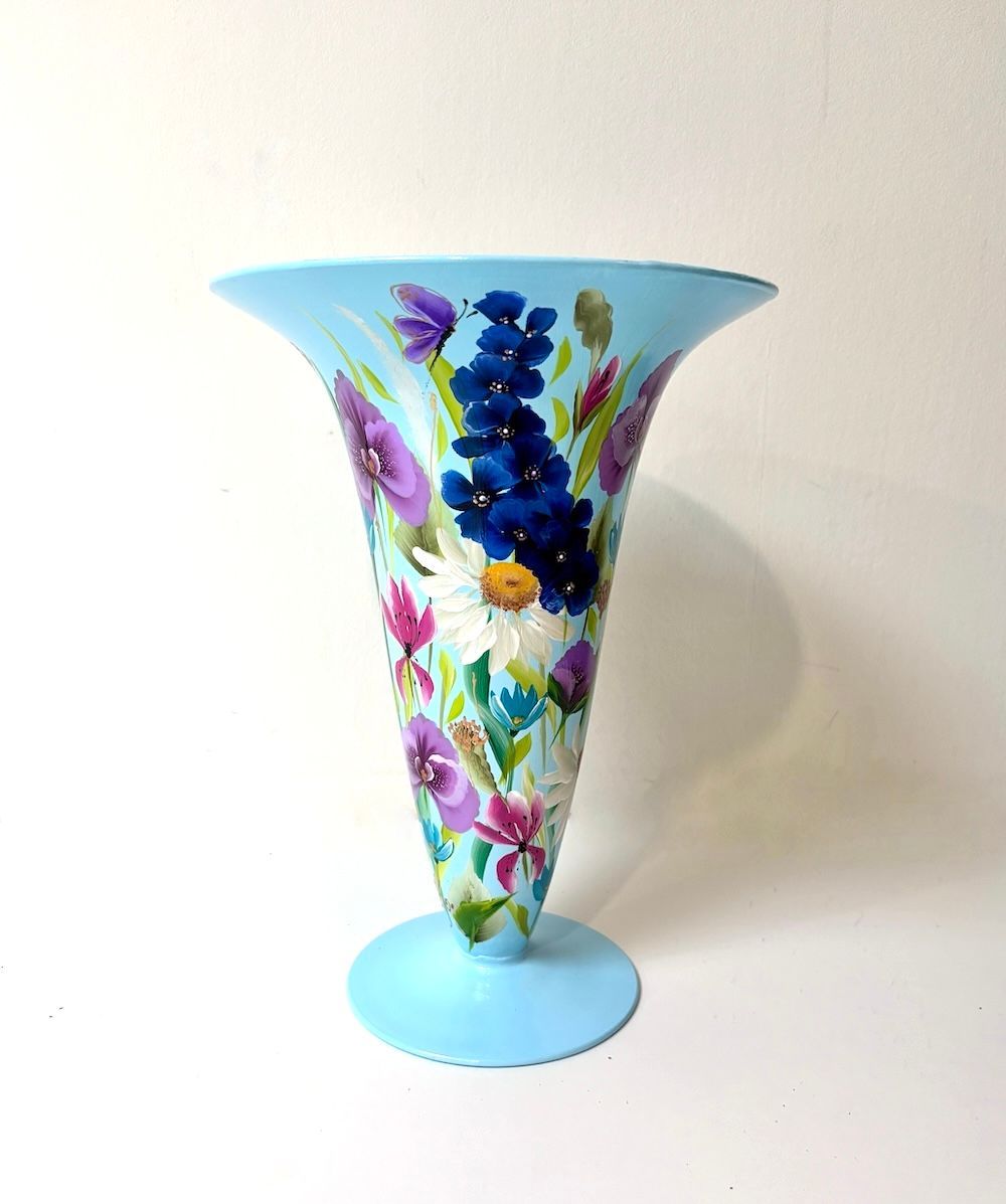 Een lichtblauwe glazen vaas met een uitlopende rand, handbeschilderd met kleurrijke wilde bloemen op een witte achtergrond.