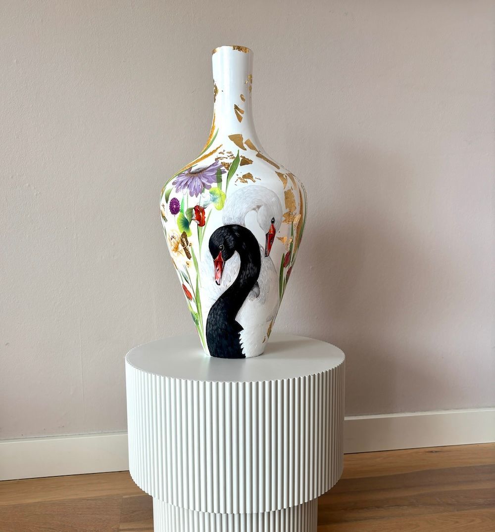 Decoratieve witte vaas met kleurrijke accenten en een zwart zwaanmotief op een gestreepte bijzettafel.