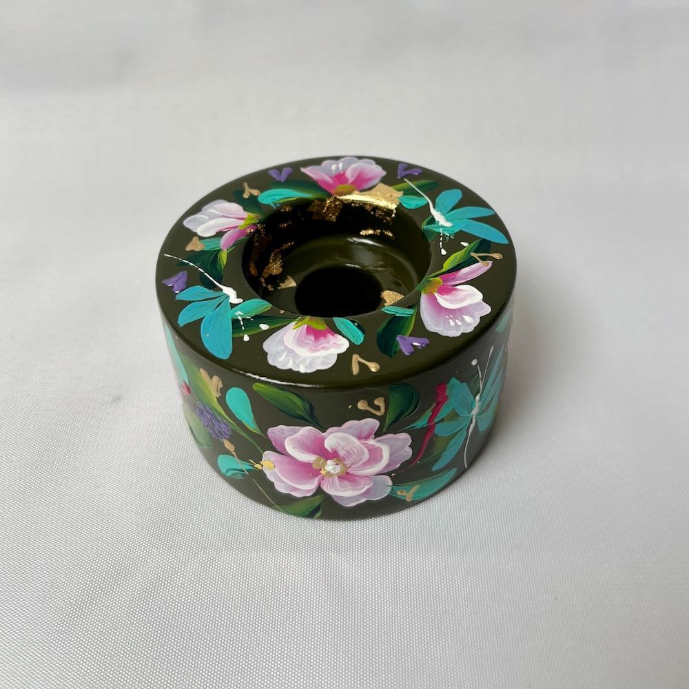 Een cilindrische, donkergroene kaarsenhouder versierd met handgeschilderde roze bloemen, groene bladeren en gouden accenten.