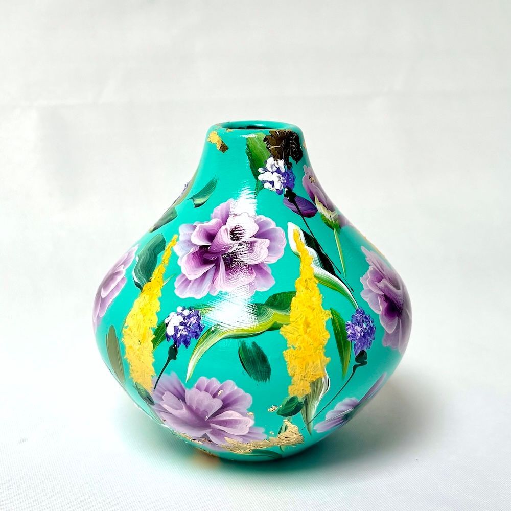 Turquoise vaas met paarse bloemen en gele accenten op een witte achtergrond.