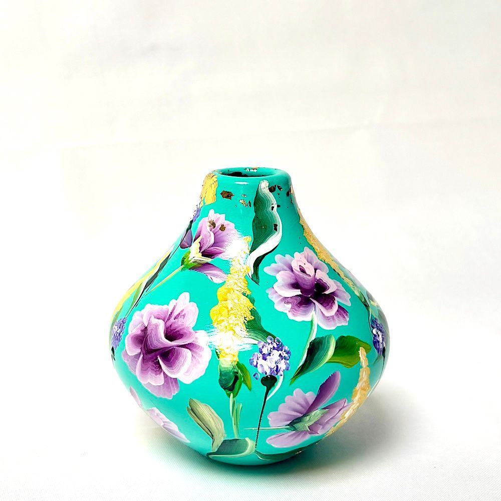 Turquoise vaas met paarse bloemen en gele accenten op een witte achtergrond.