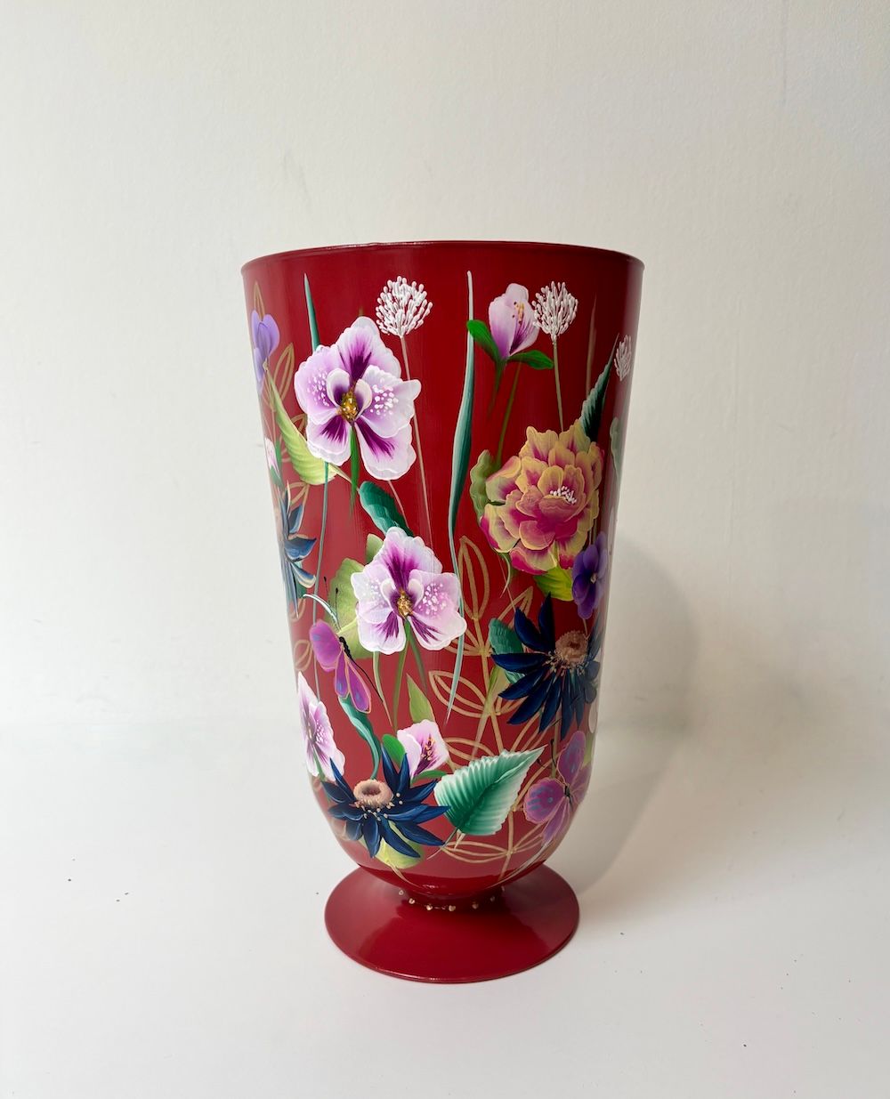 Een hoge, rode vaas op een voetstuk, geschilderd met een levendige, iriserende kolibrie omringd door kleurrijke bloemen.