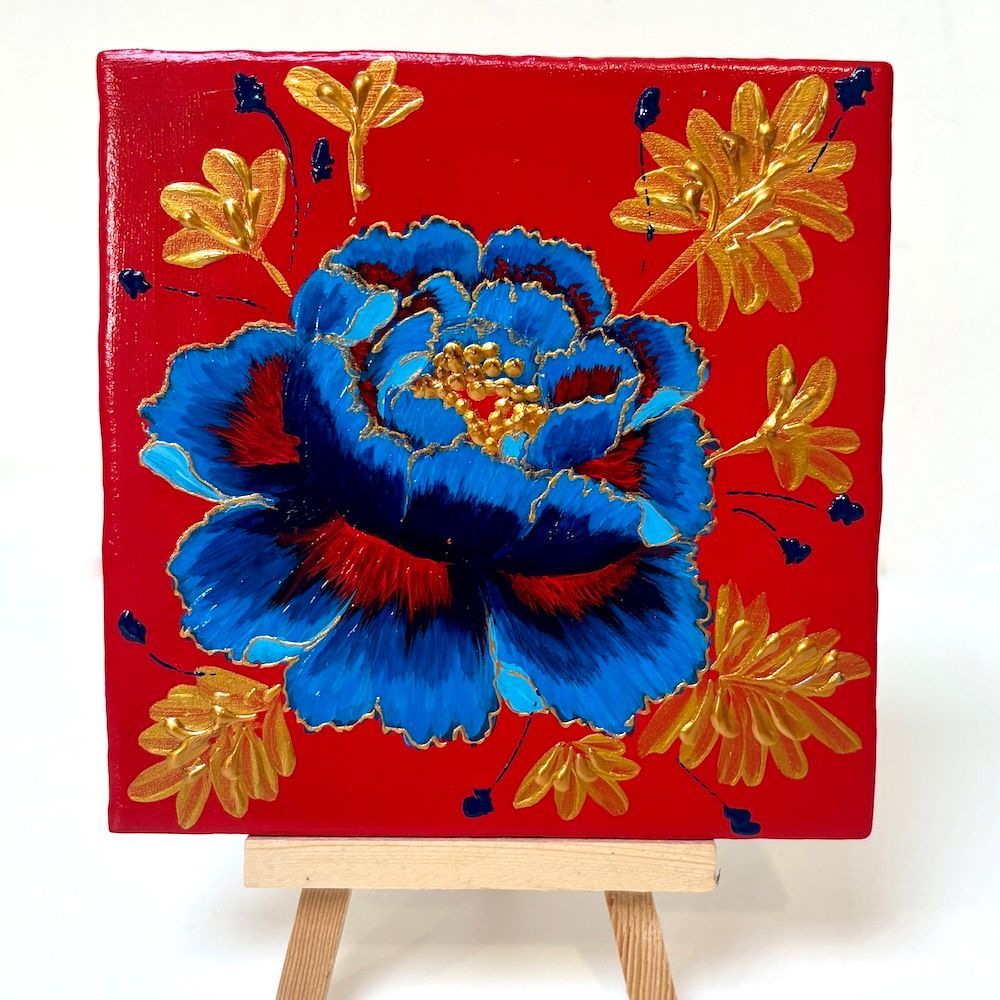 Decoratieve blauwe bloem op rood canvas met gouden bladeren, tentoongesteld op een kleine schildersezel.