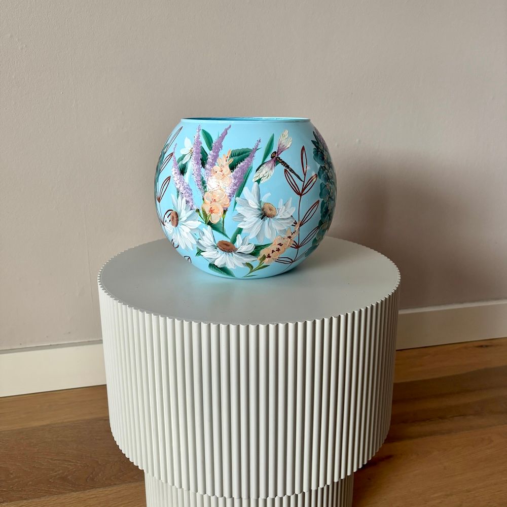 Blauwe vaas met paarse bloemen op een geribbelde witte sokkel.