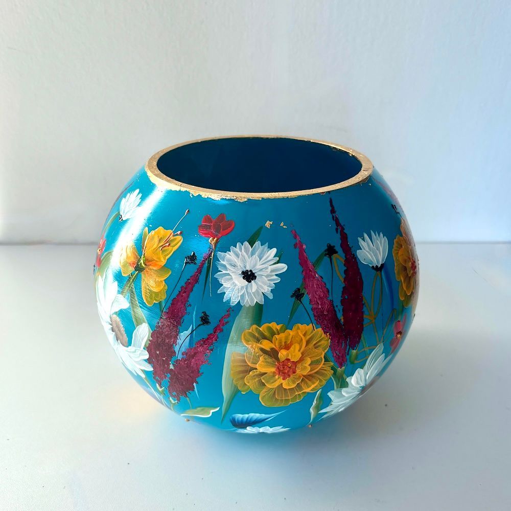Een ronde, turquoise vaas, beschilderd met levendige, veelkleurige bloemenpatronen en afgewerkt met een goudkleurige rand.