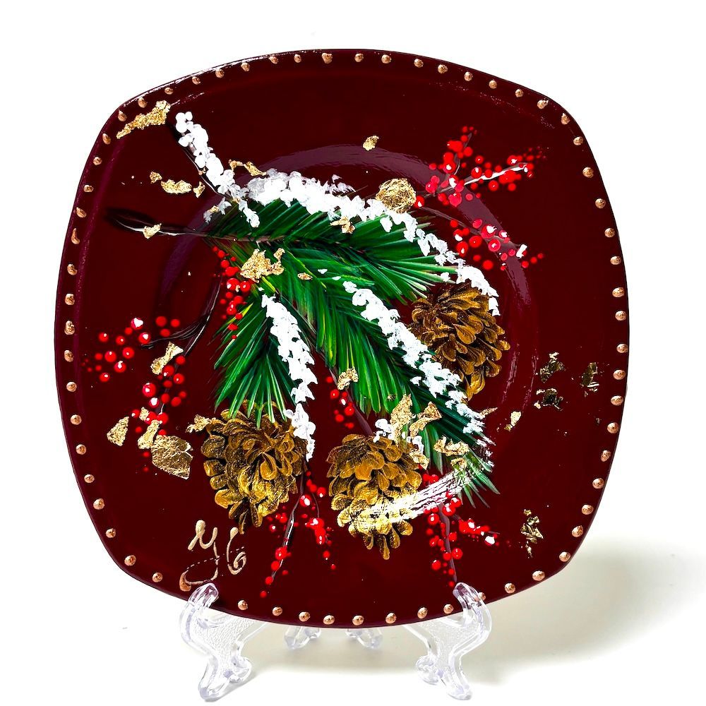 Decoratief rood vierkant bord met groene hulstbladeren en gouden accenten op een transparante standaard.