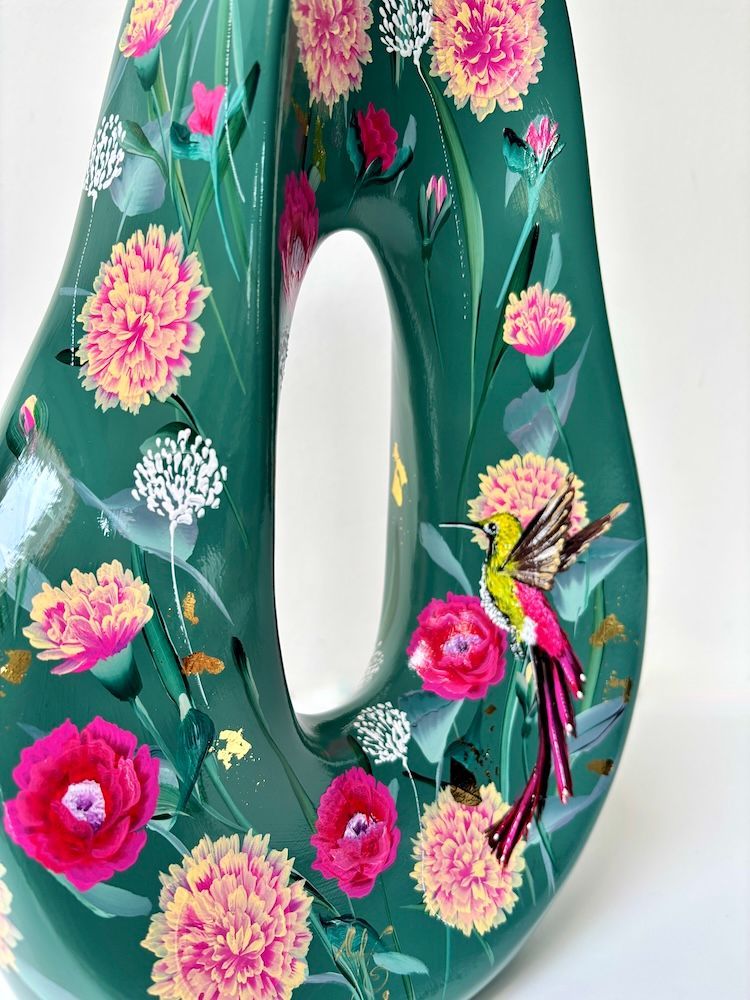 Een peervormige donkergroene vaas met een uitsparing in het midden, beschilderd met roze bloemmotieven en een klein vogeltje.