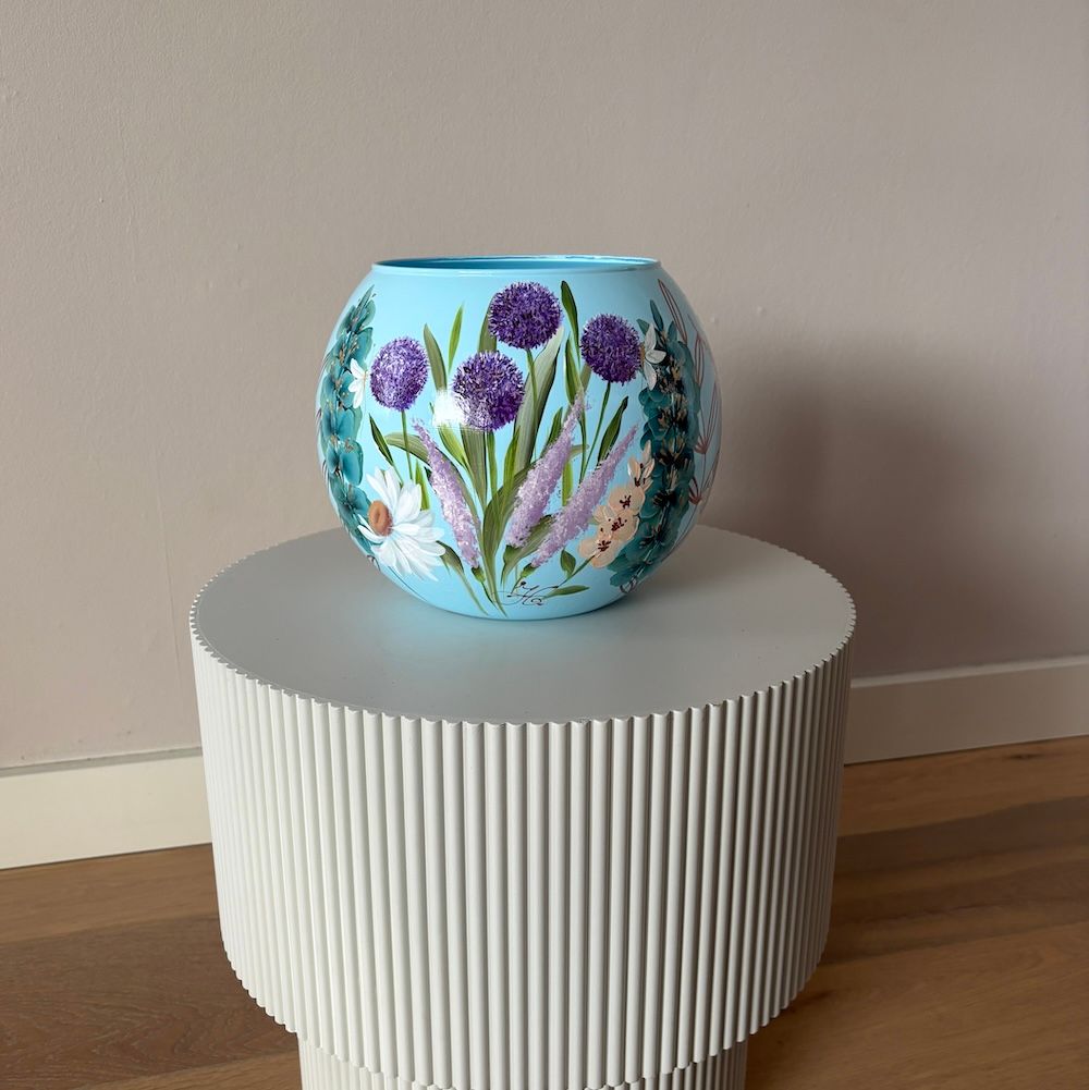Blauwe vaas met paarse bloemen op een geribbelde witte sokkel.