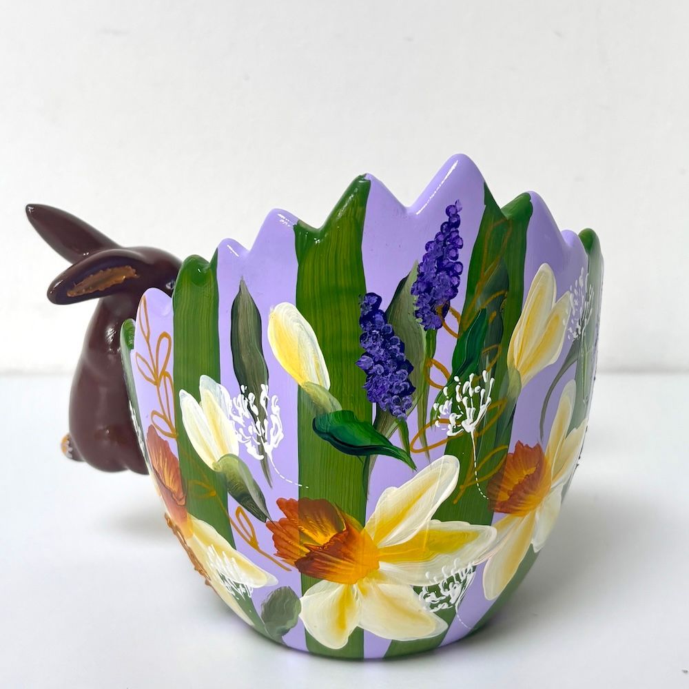Twee chocoladekonijntjes naast een paarse paasmand met bloemen.
