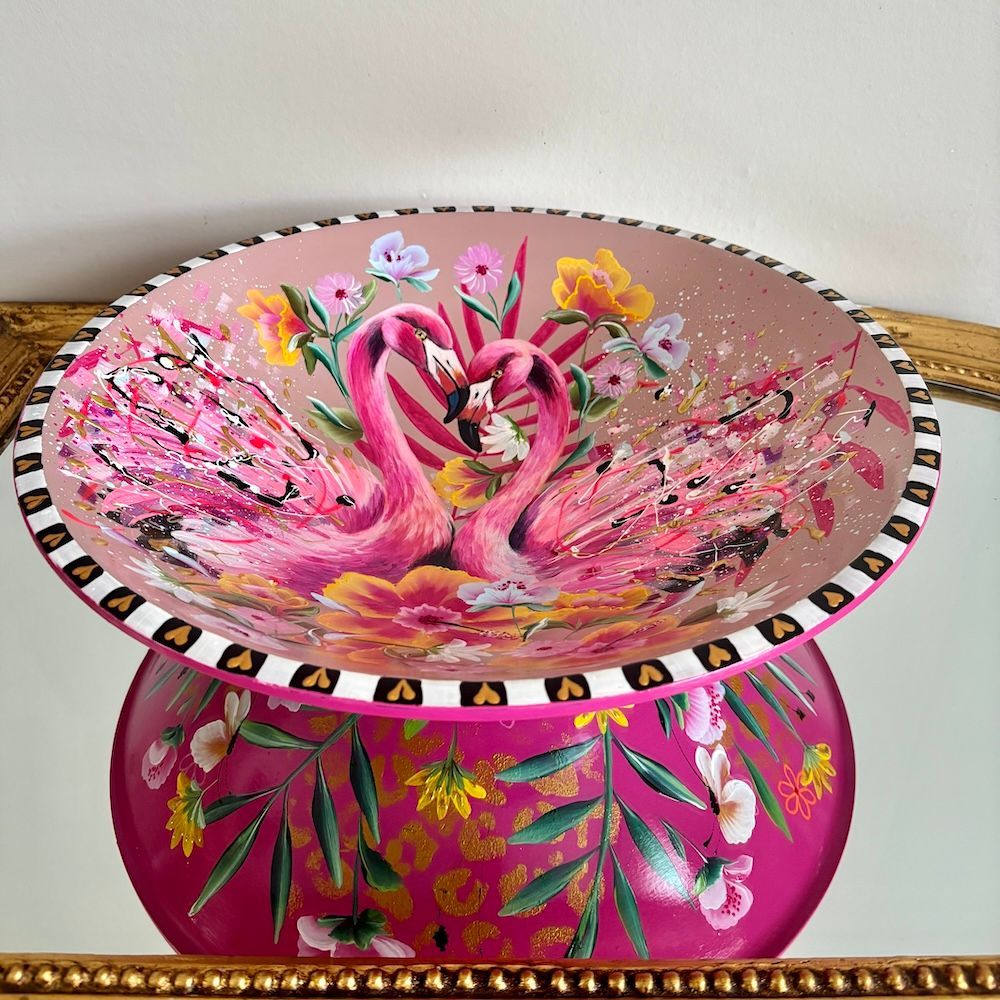 Decoratieve glazen schaal in de vorm van een roze flamingo met bloemen- en tropische patronen op een bijpassende standaard.