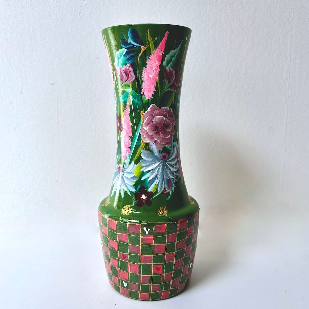 Decoratieve groene vaas met roze bloemen- en ruitpatronen op een witte achtergrond.