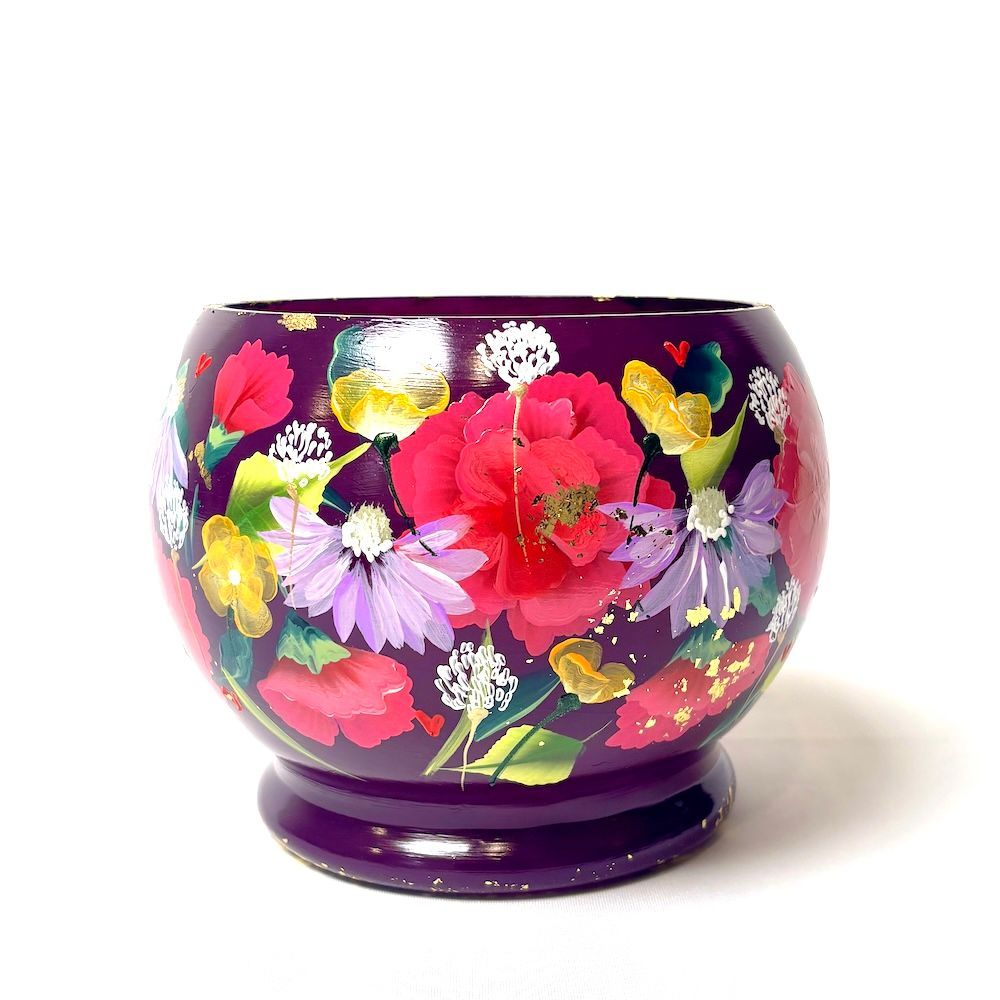 Een donkerpaarse, bolvormige houten schaal met handgeschilderde kleurrijke bloemen, rustend op een voetstuk.