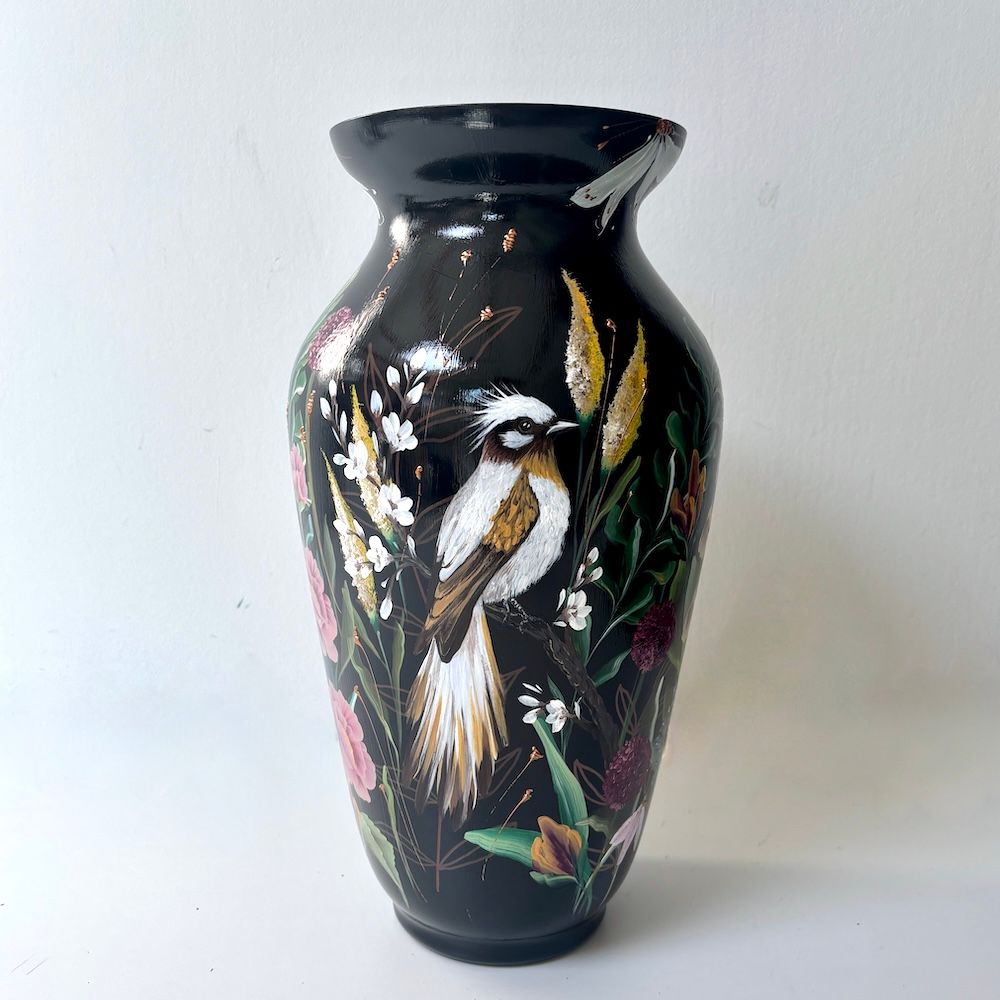 Zwarte vaas met een geschilderde vogel en bloemenmotief op een lichte achtergrond.