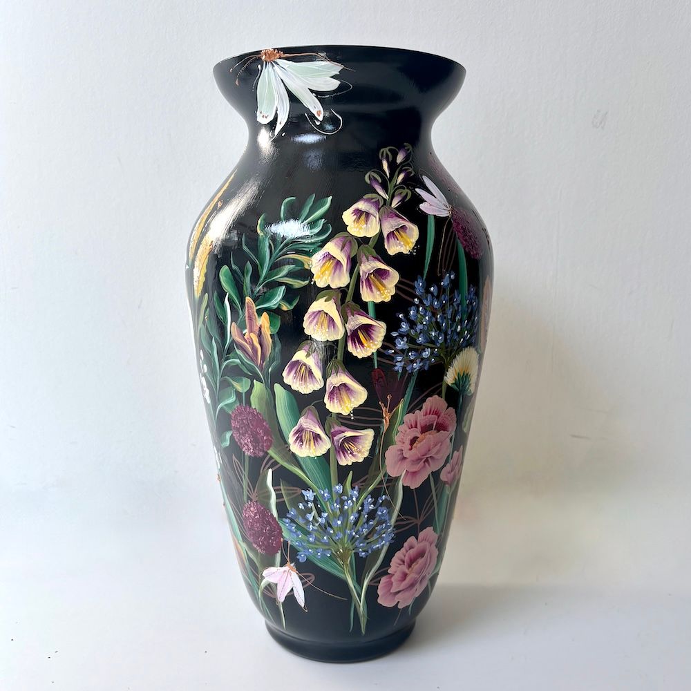 Zwarte vaas met een geschilderde vogel en bloemenmotief op een lichte achtergrond.