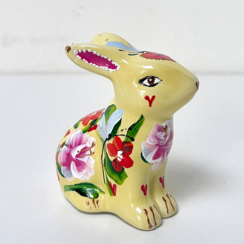 Geel keramisch konijnenbeeldje met bloemen in roze, rode en groene tinten.