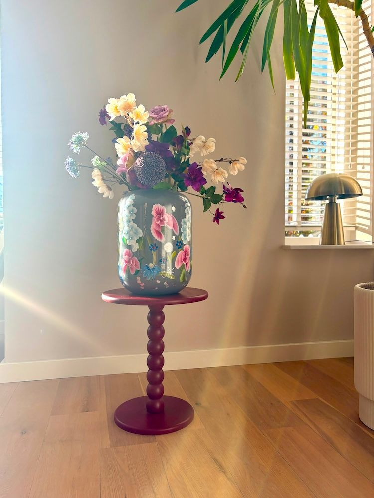 Decoratieve grijze vaas beschilderd met kleurrijke bloemen op een zwarte standaard.