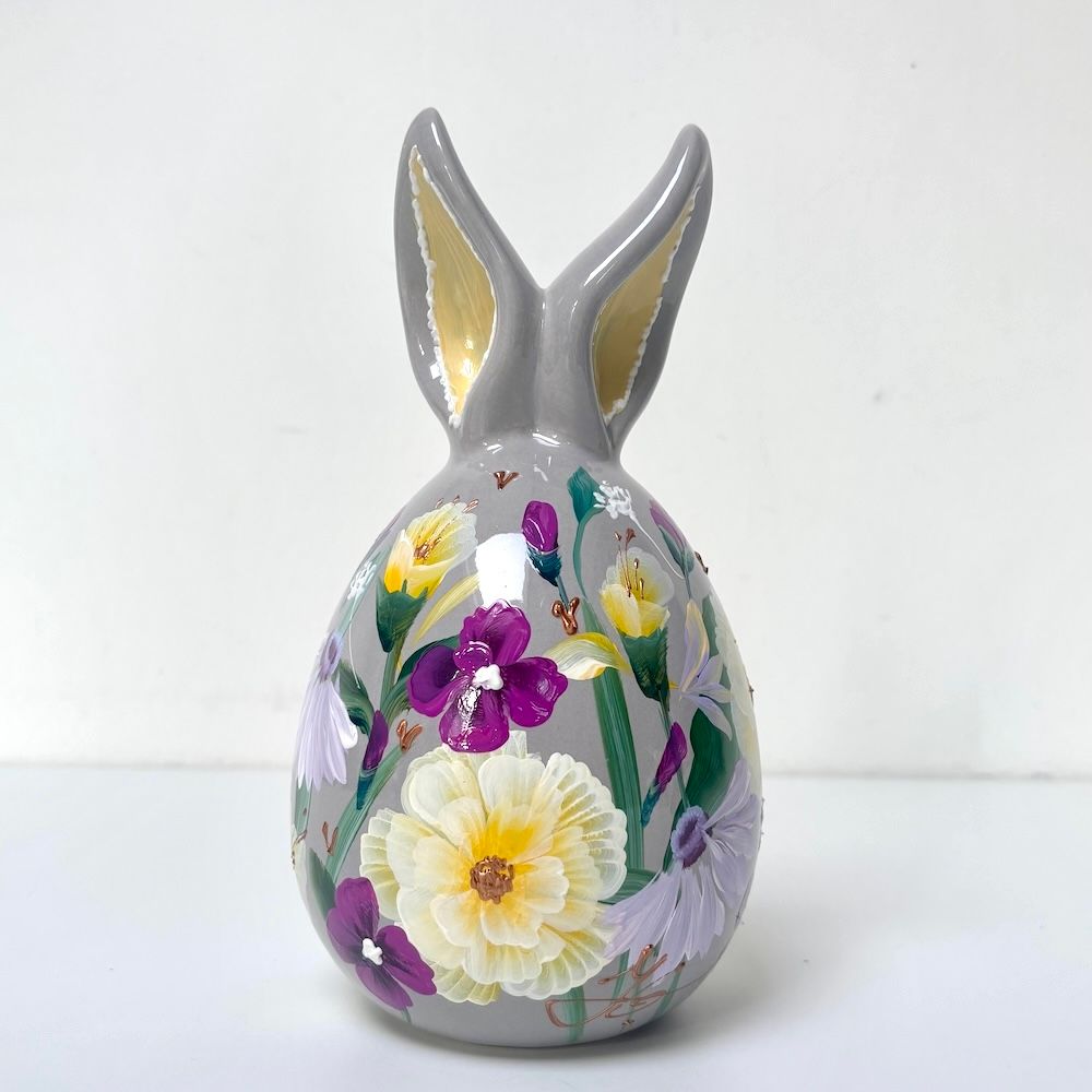 Grijze keramische konijnenfiguur met handgeschilderde bloemmotieven in geel, paars en groen.