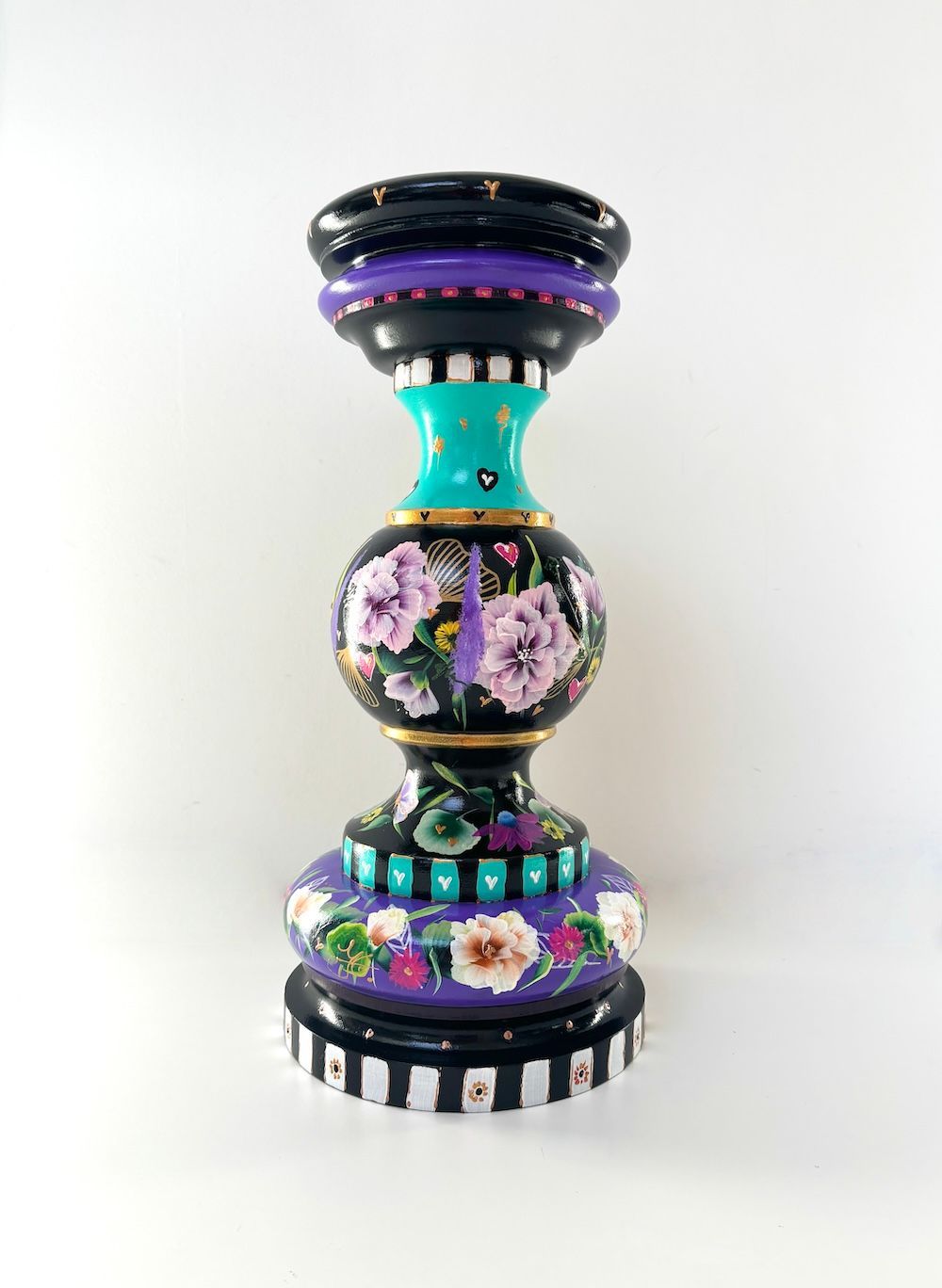 Een decoratieve, handbeschilderde houten kaarsenhouder met bloemen, opvallende strepen en paarse en turquoise tinten.