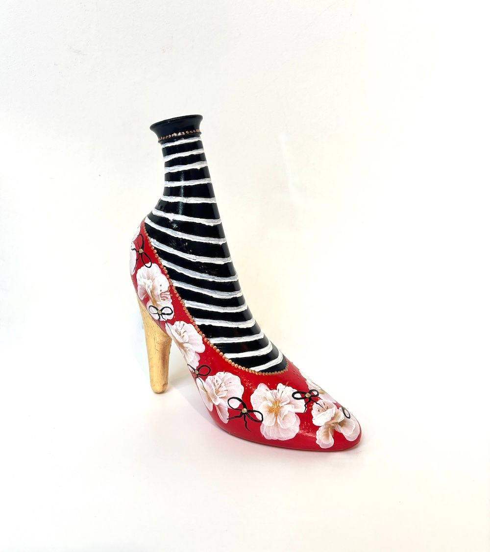 Decoratieve rode schoen met bloemenprint en hoge hak, met een zwart-wit gestreept bovenwerk en een gouden hak.